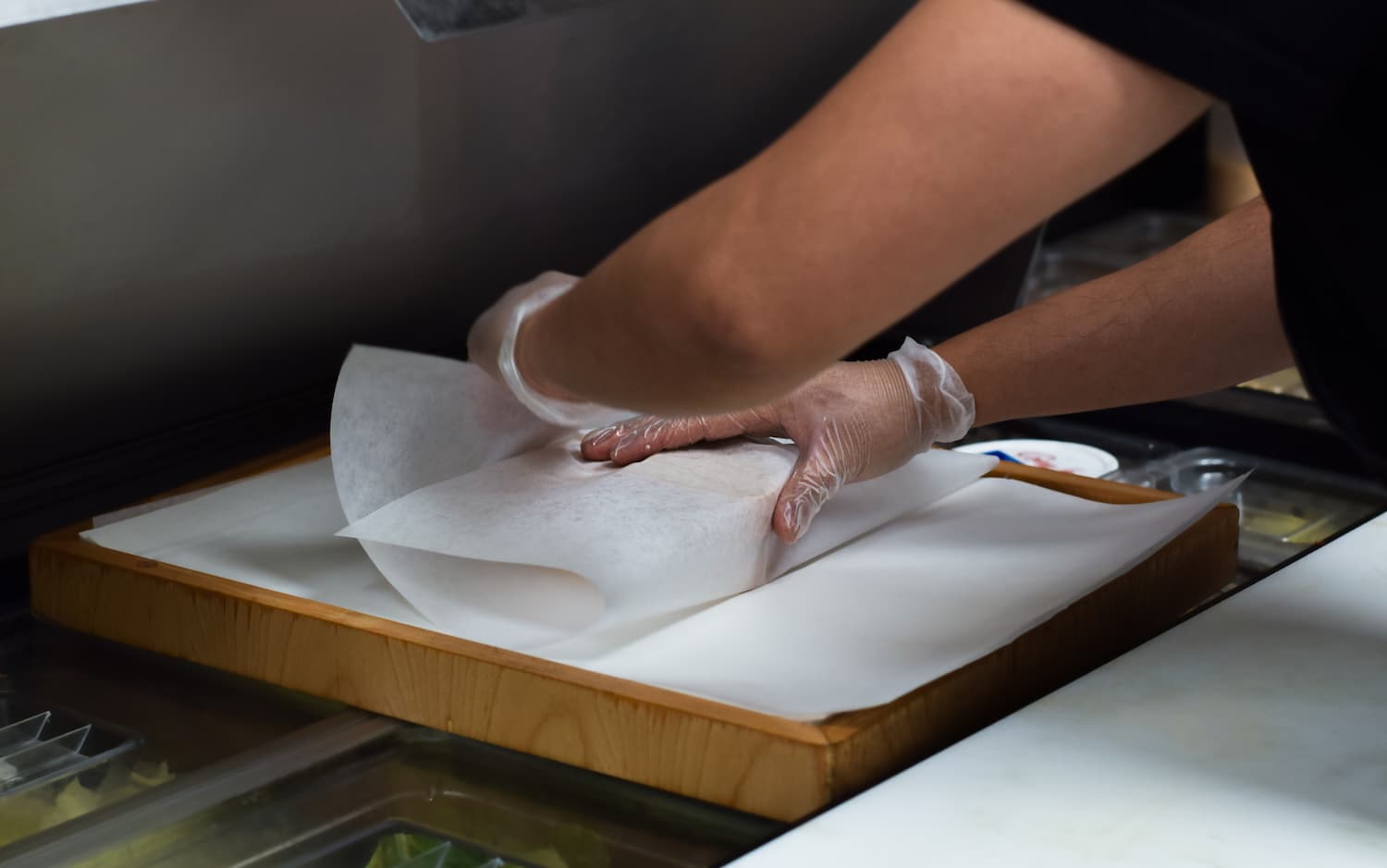 restaurant kitchen employee wraps a sandwich in dry wax paper